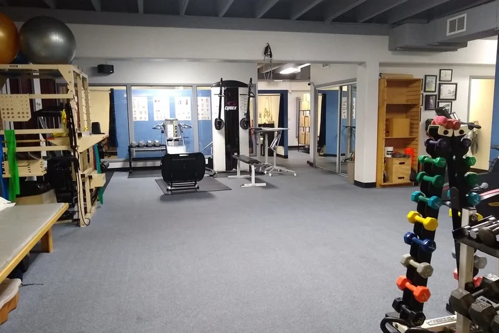 The Action Rehab treatment floor: open carpeted space with a cable machine, a weight bench, dumbbell racks, resistance bands and exercise balls