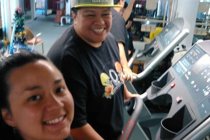 Two people smiling beside a treadmill on the Action Rehab clinic floor during a session