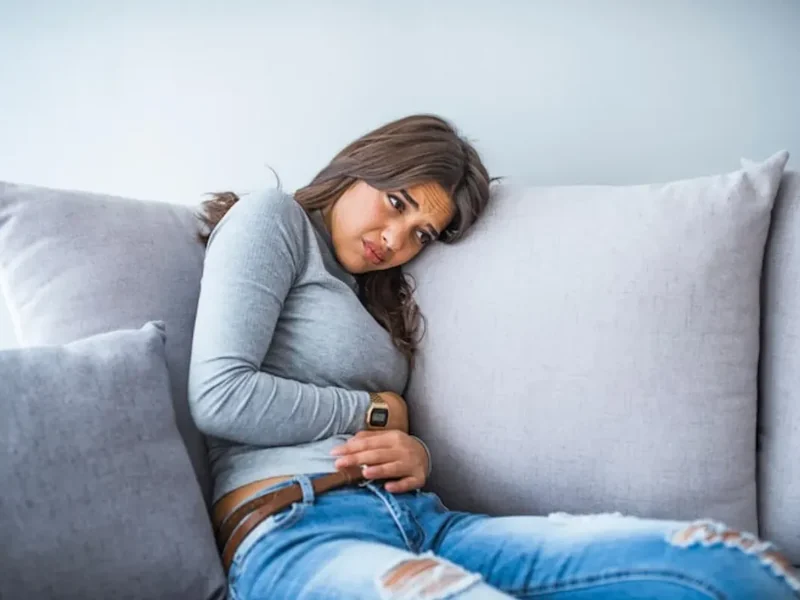 Woman resting on a couch with her hand pressed against her lower abdomen